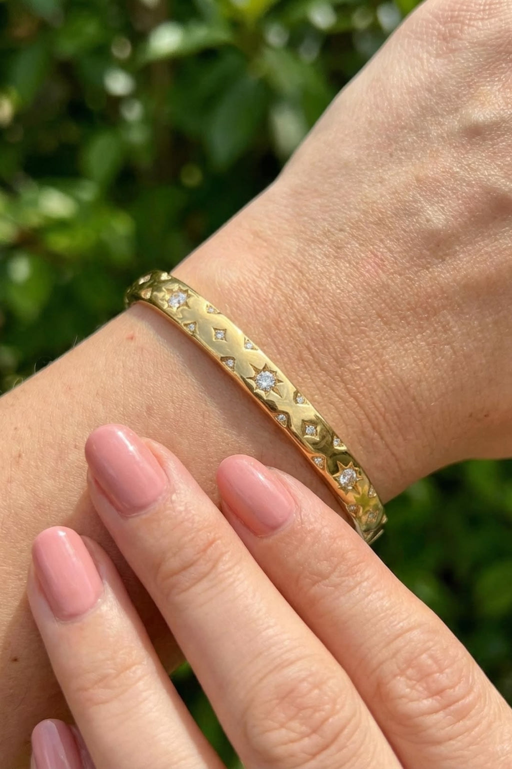 Gold bracelet with embedded stones on a wrist against a blurred green background