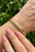 Gold bracelet with embedded stones on a wrist against a blurred green background