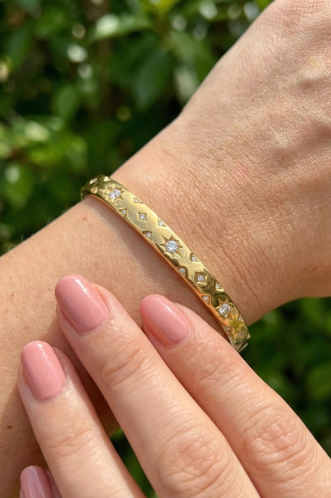 Gold bracelet with embedded stones on a wrist against a blurred green background