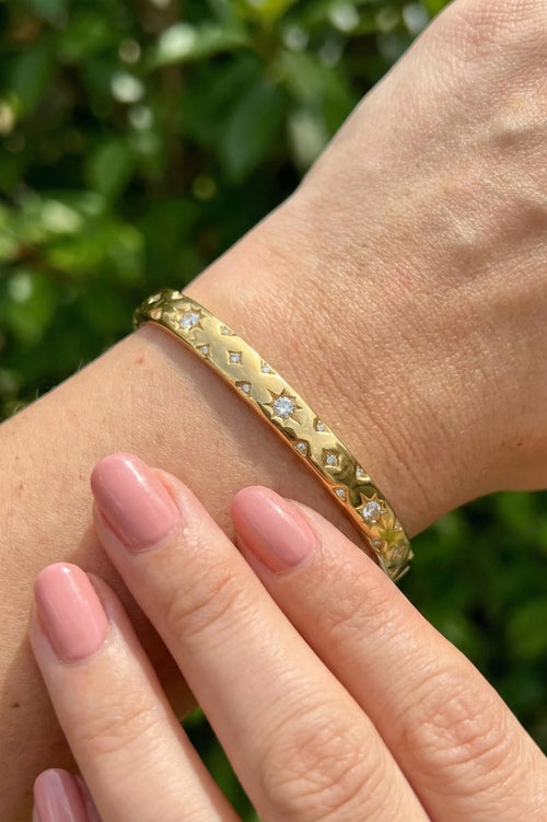 Gold bracelet with embedded stones on a wrist against a blurred green background