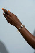 Hand wearing a gold bracelet with clear stones against a light blue background