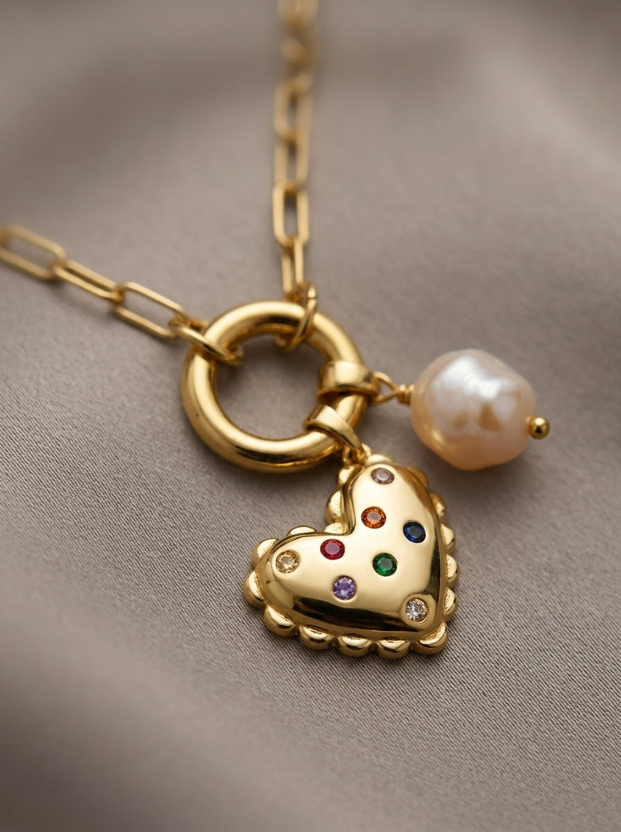 Gold necklace with a heart-shaped pendant and pearl charm on a neutral background