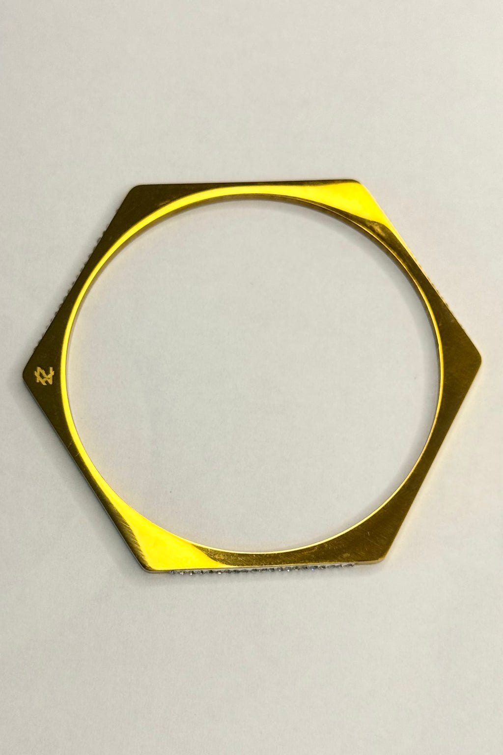 A gold-toned hexagonal metal ring or frame with a circular cutout, photographed on a plain light background.