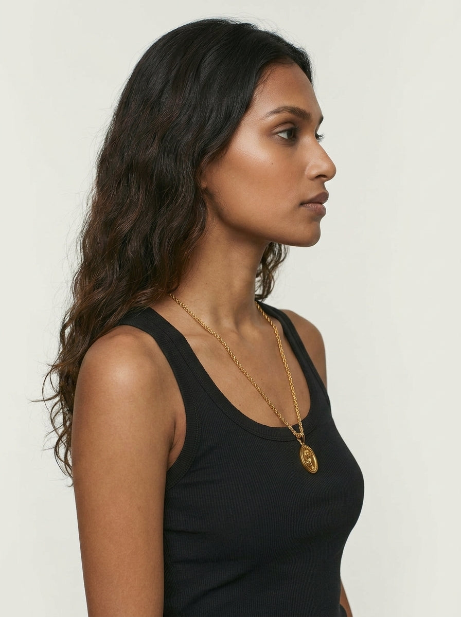 Woman wearing a black tank top and gold necklace against a white background