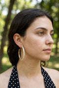 Woman wearing gold hoop earrings with a blurred green outdoor background