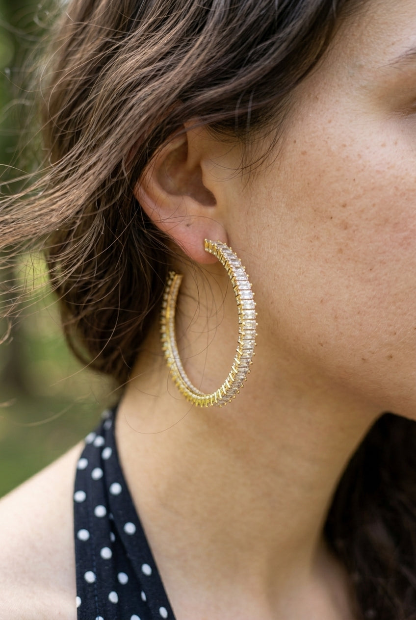 Close-up of a person wearing gold hoop earrings with a blurred natural background