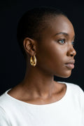 Woman wearing gold hoop earrings against a black background