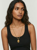 Woman wearing a gold necklace with a pendant on a plain background
