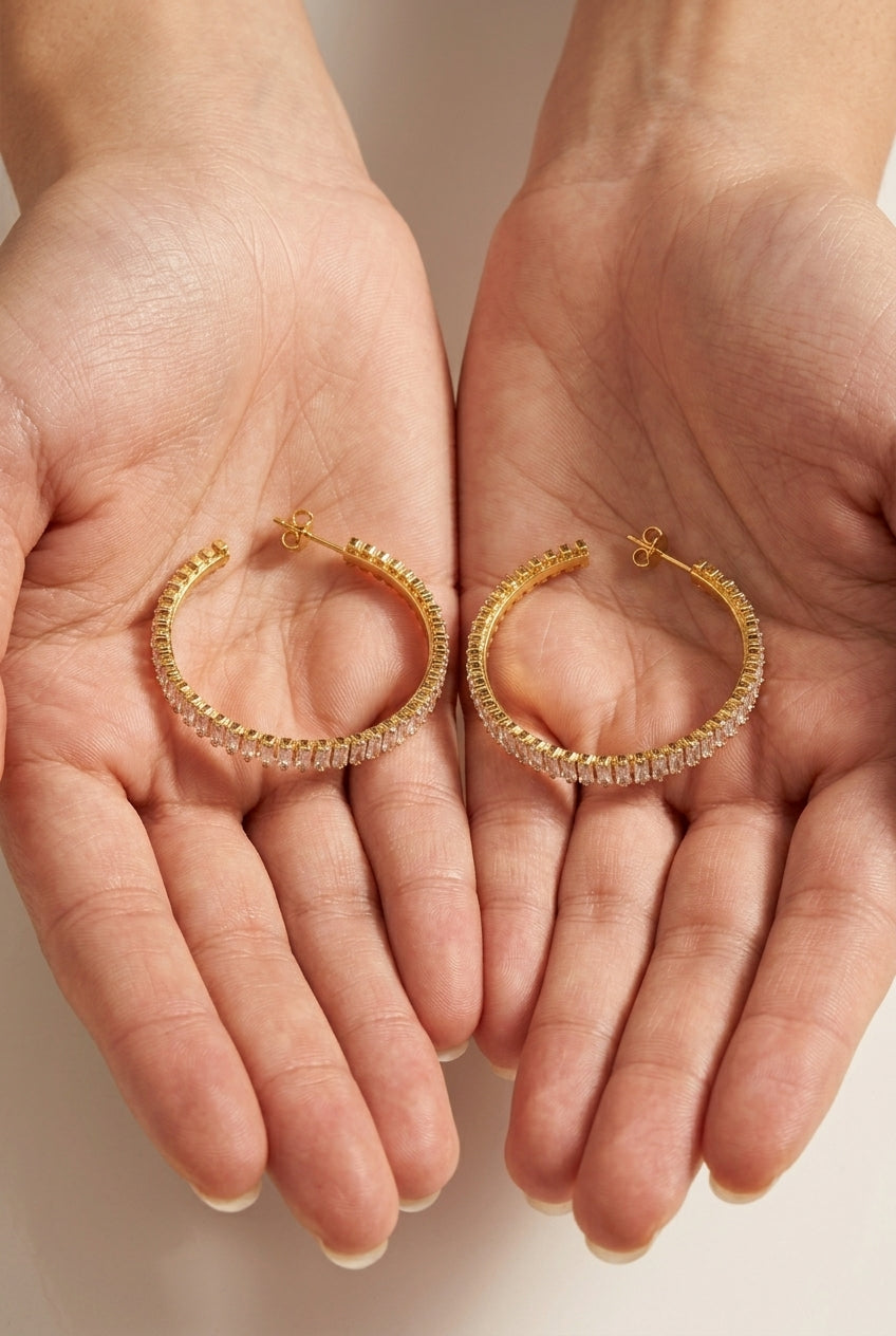 Gold hoop earrings held in two hands against a neutral background