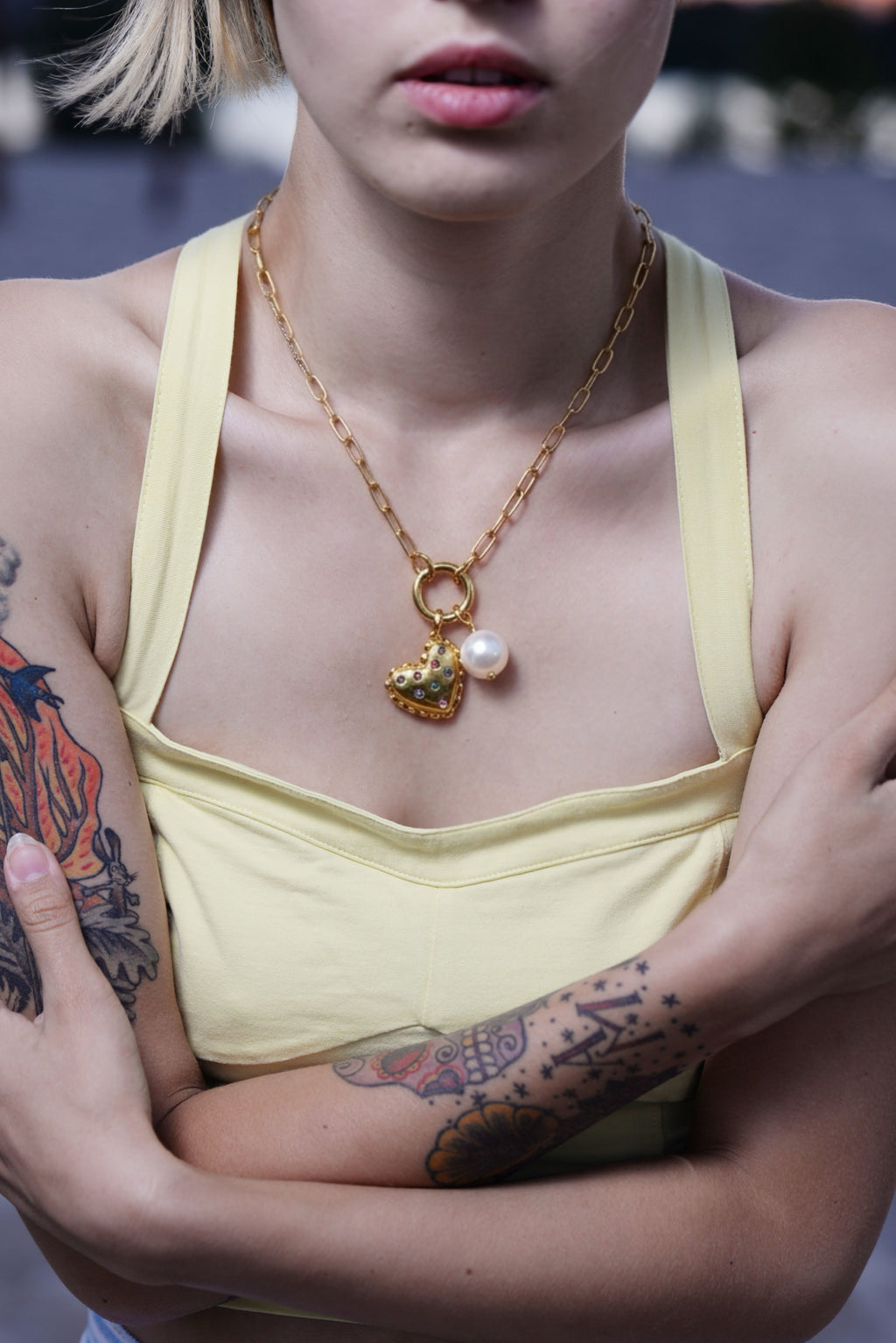 Person wearing a yellow tank top with a gold necklace featuring a heart-shaped pendant.